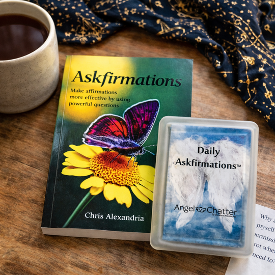 Book titled 'Askfirmations' with a butterfly and flower on the cover, next to a deck of cards titled 'Daily Askfirmations' on a wooden surface.